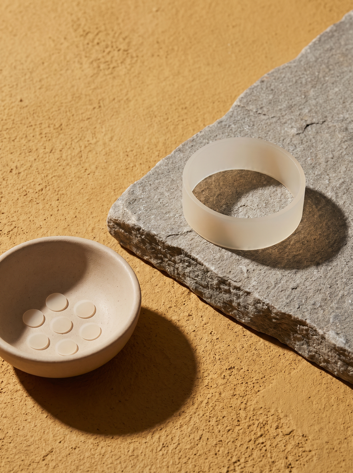One wide hydrocolloid band on a stone slab beside a small dish of tiny round dots on a golden ochre surface
