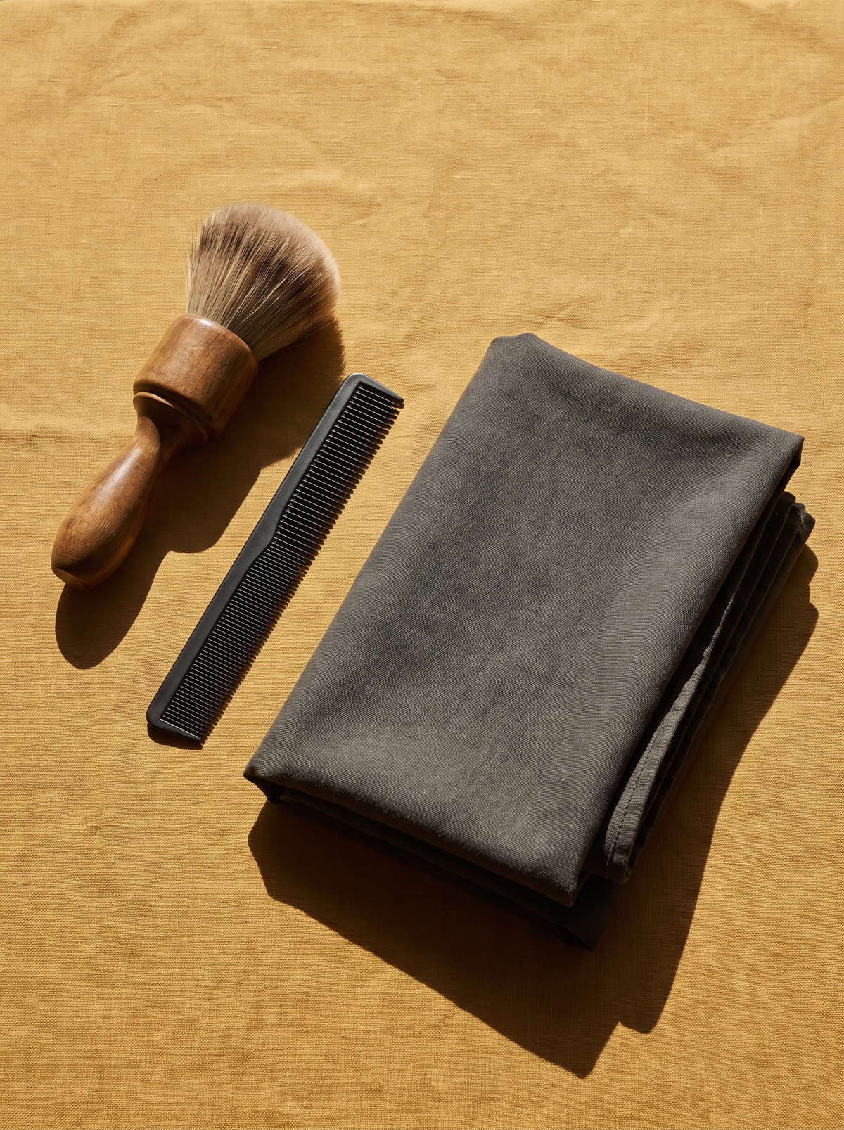 A barber's neck brush, a cutting comb and a folded cape on a golden ochre surface