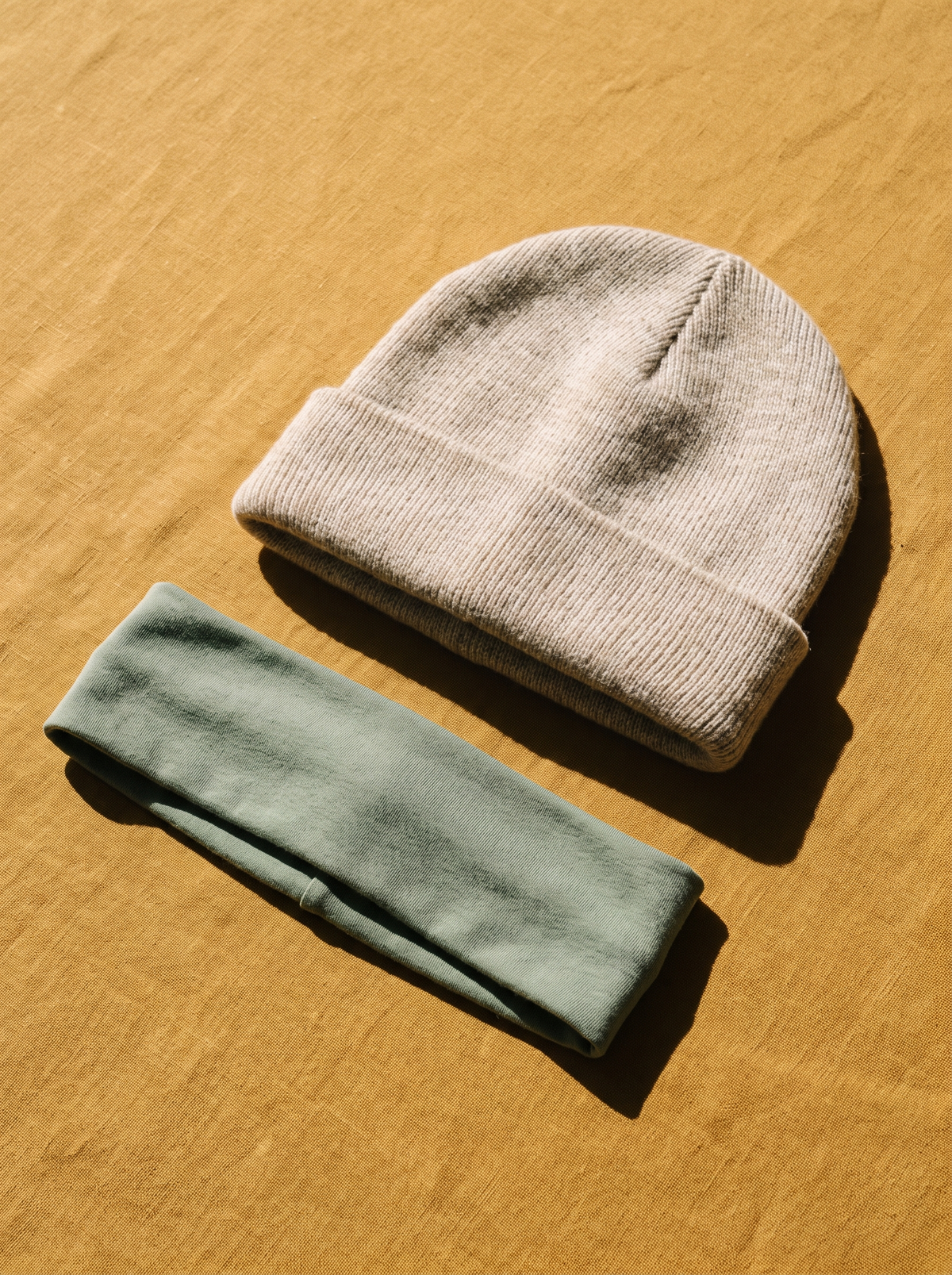 A knit beanie and a fabric headband on a golden ochre surface