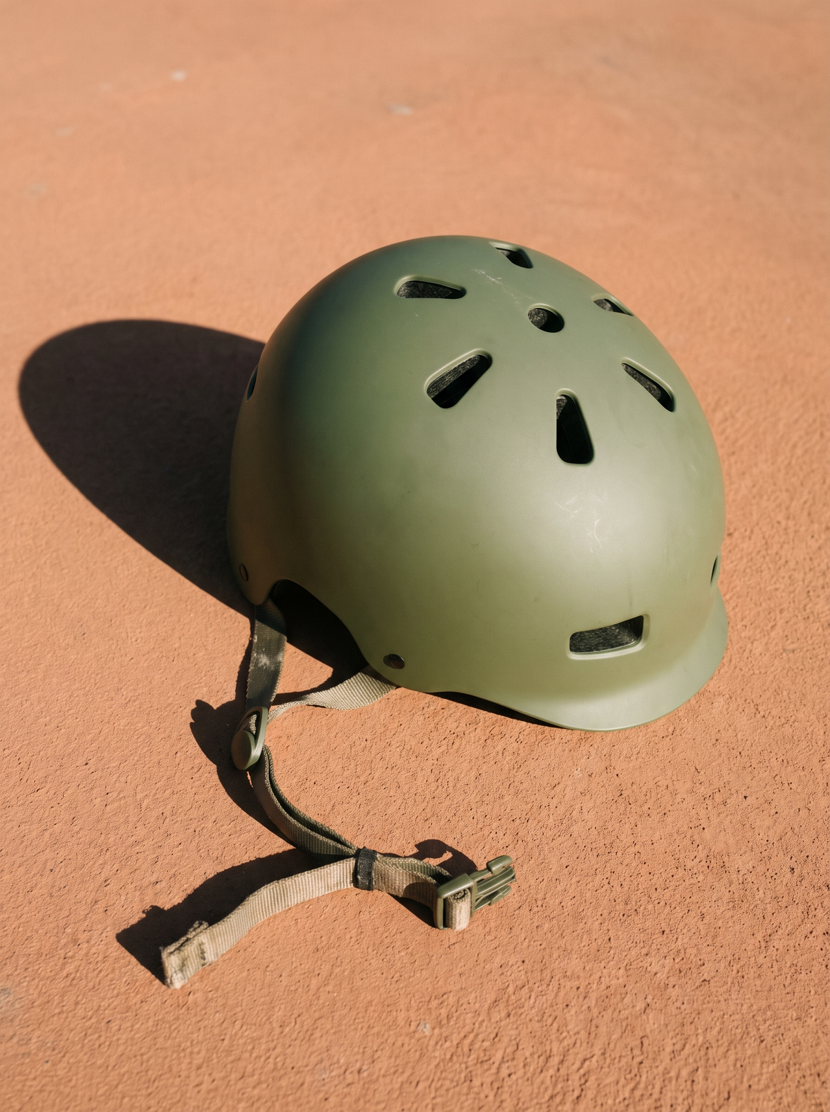 A bicycle helmet on its side with the chin strap unbuckled on a terracotta surface