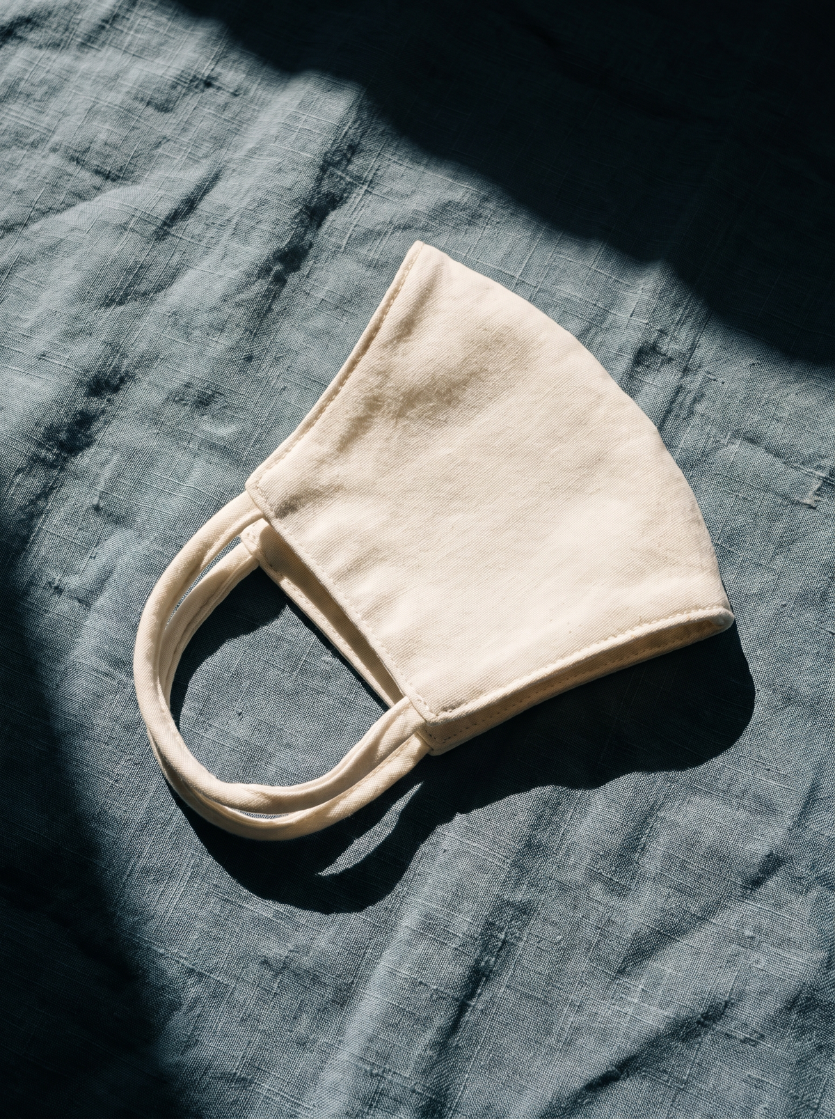 A plain cotton face mask laid on dusty-blue linen