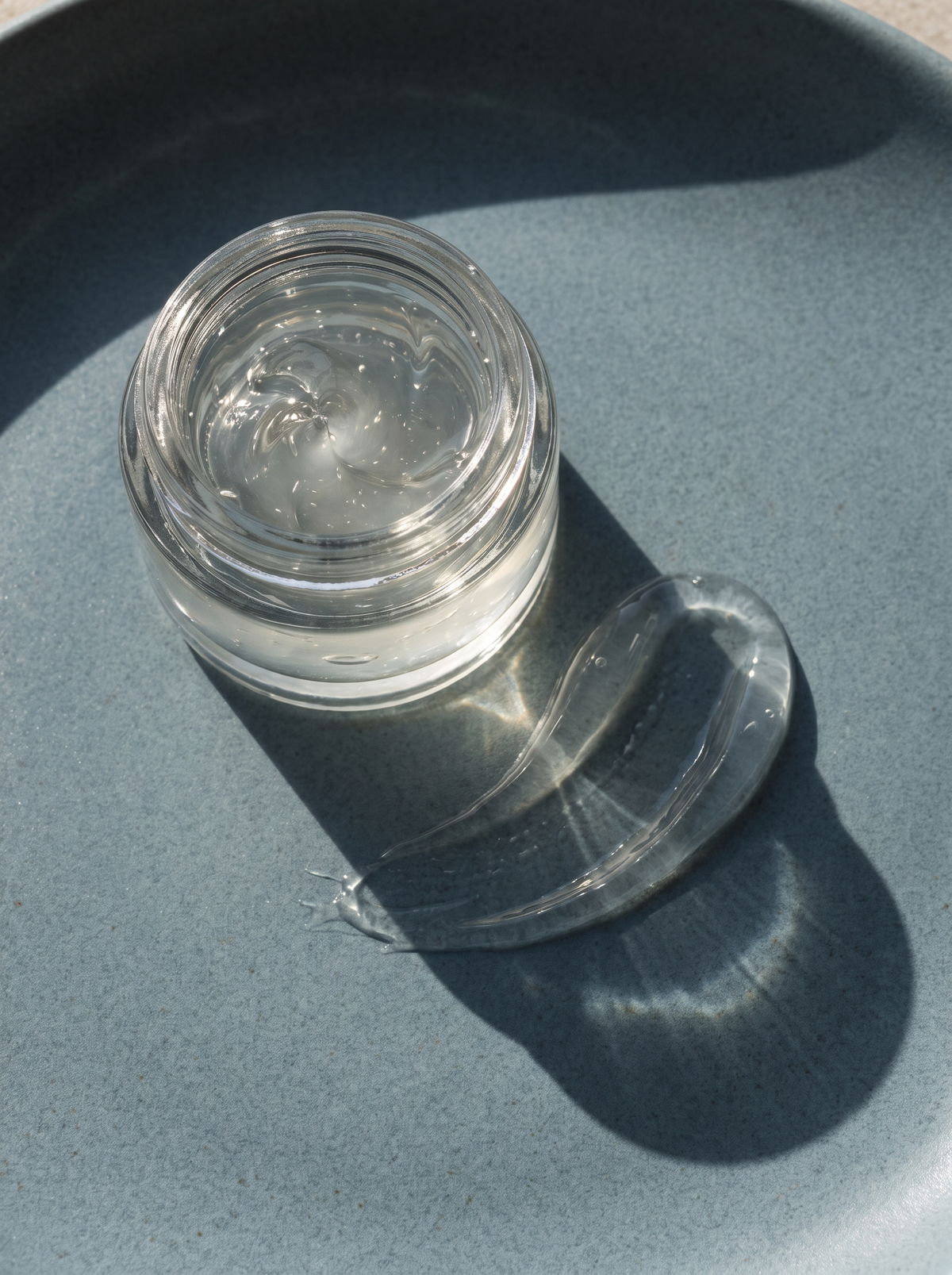 A small open jar of gel moisturizer with a swipe of gel on a dusty-blue surface