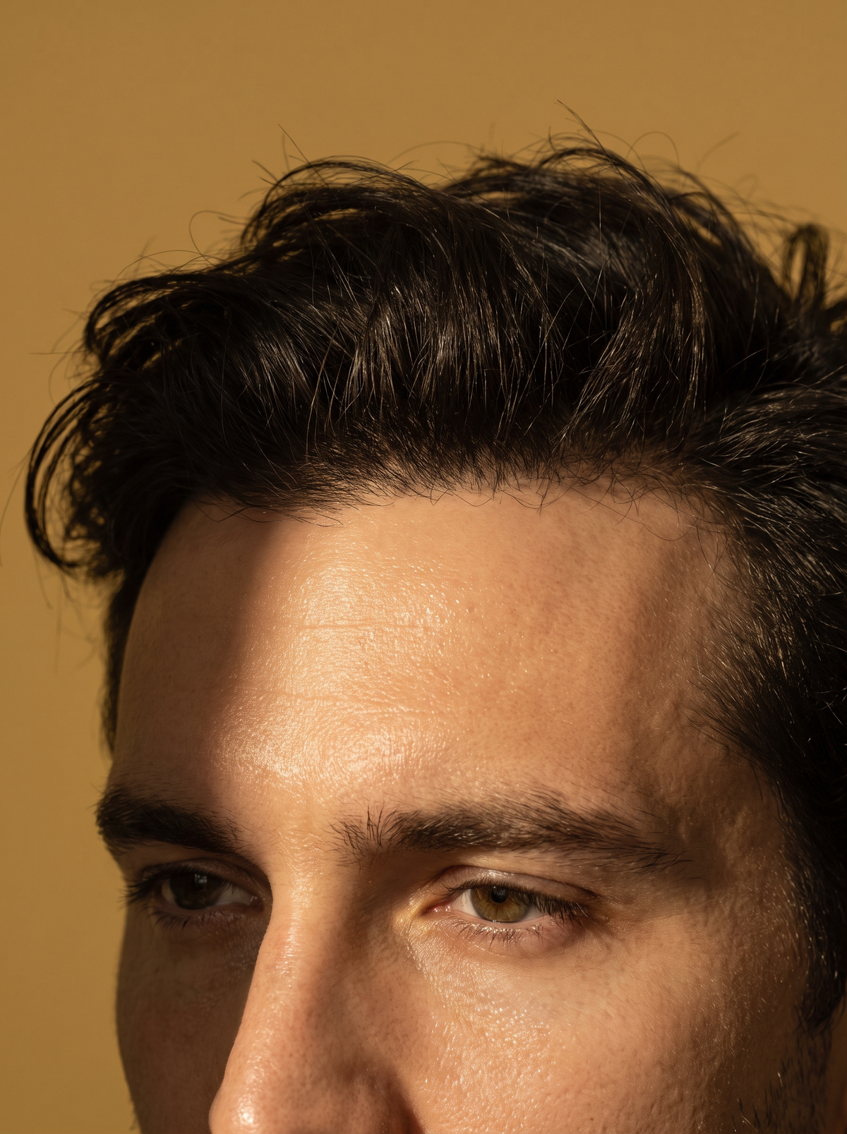 Close-up of an adult man's forehead and brow with natural skin in golden ochre light, the wide zone that sweats during a workout