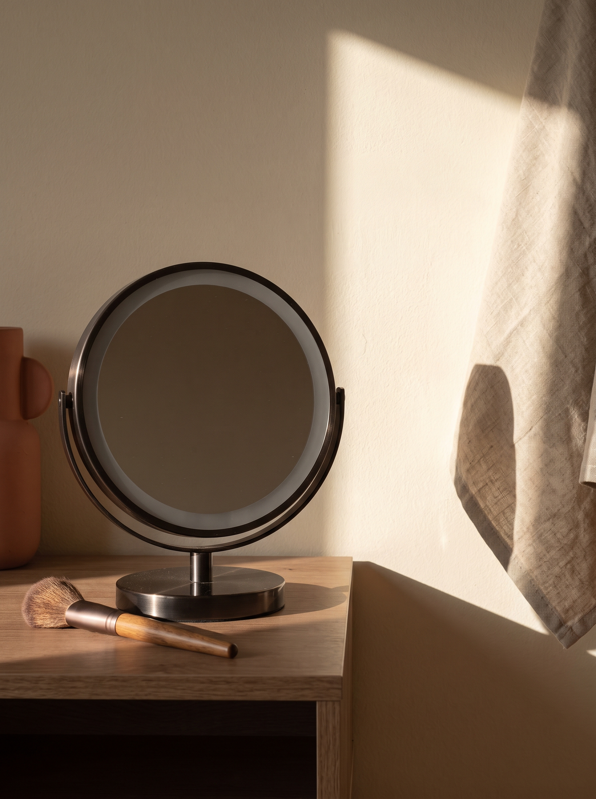 A small ring light switched off on a tidy vanity with one makeup brush