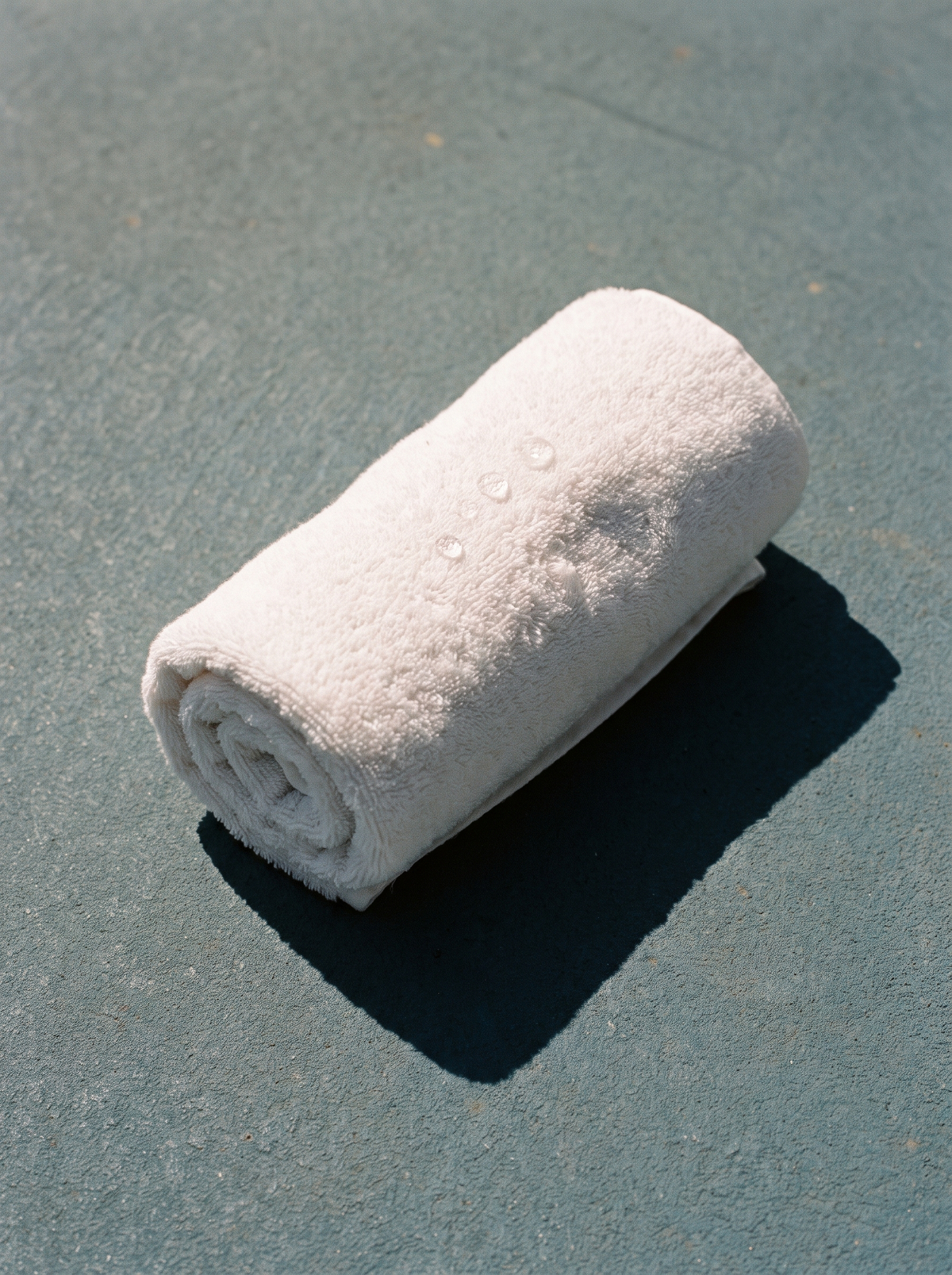 A rolled white cotton gym towel with beads of water on a dusty-blue surface