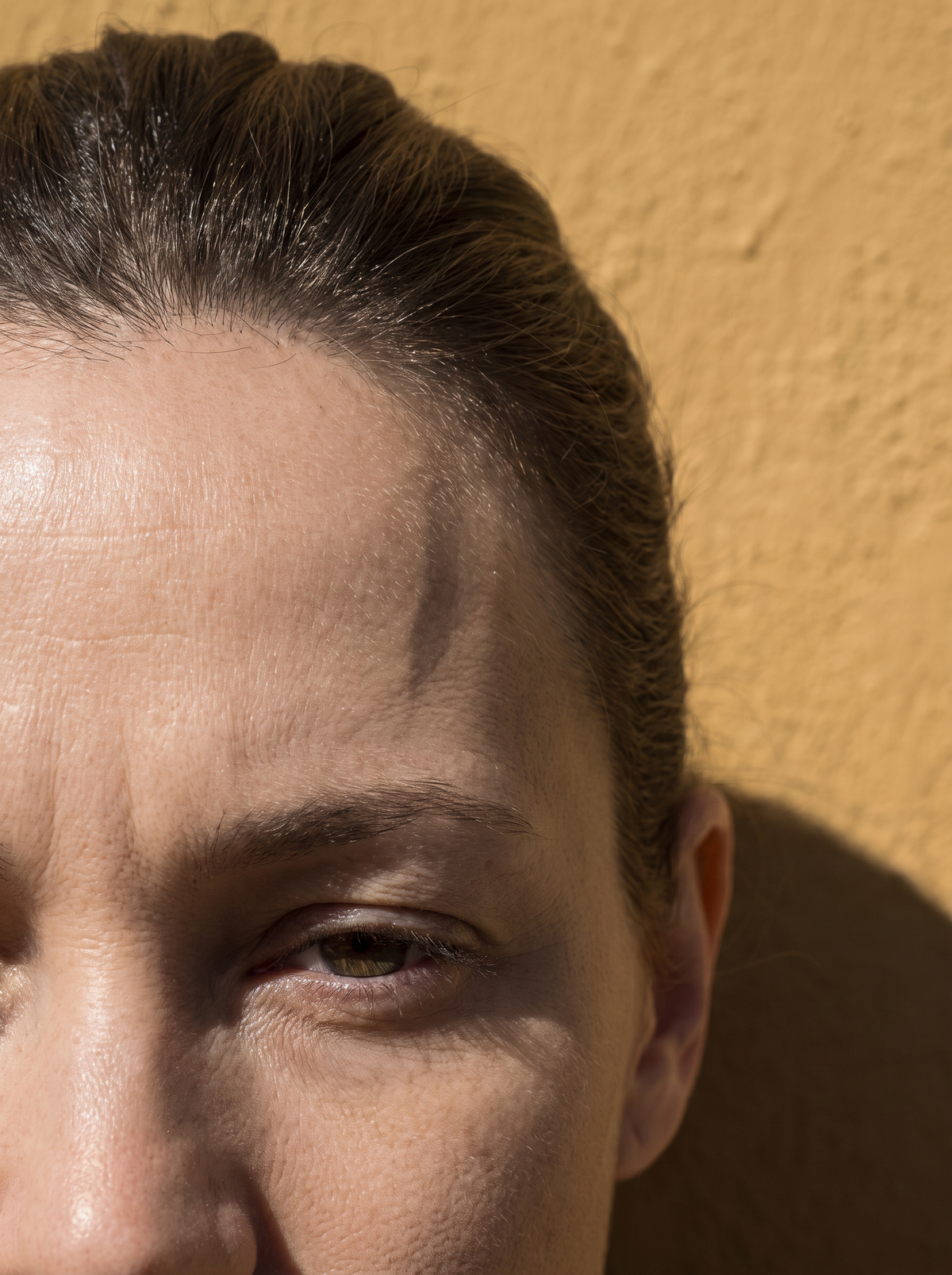 Close-up of an adult woman's forehead and brow with natural skin on a golden ochre background