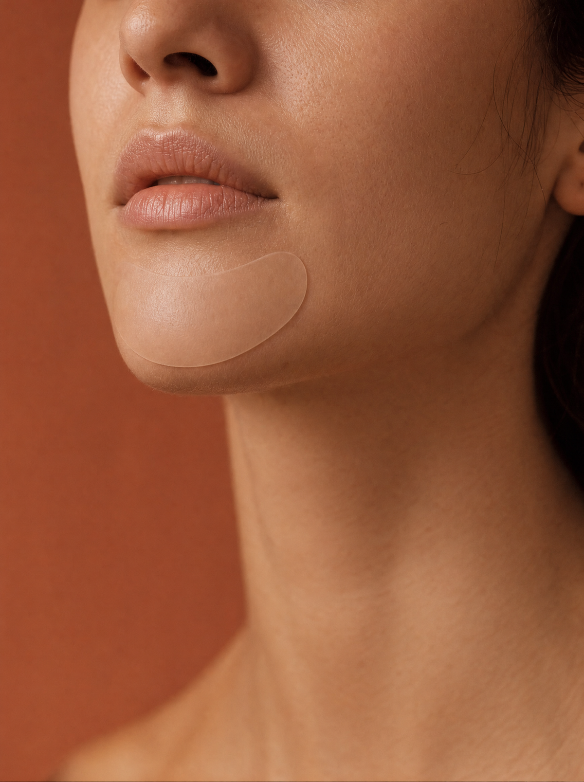 The Chin Patch worn along the jaw, close-up on a terracotta background